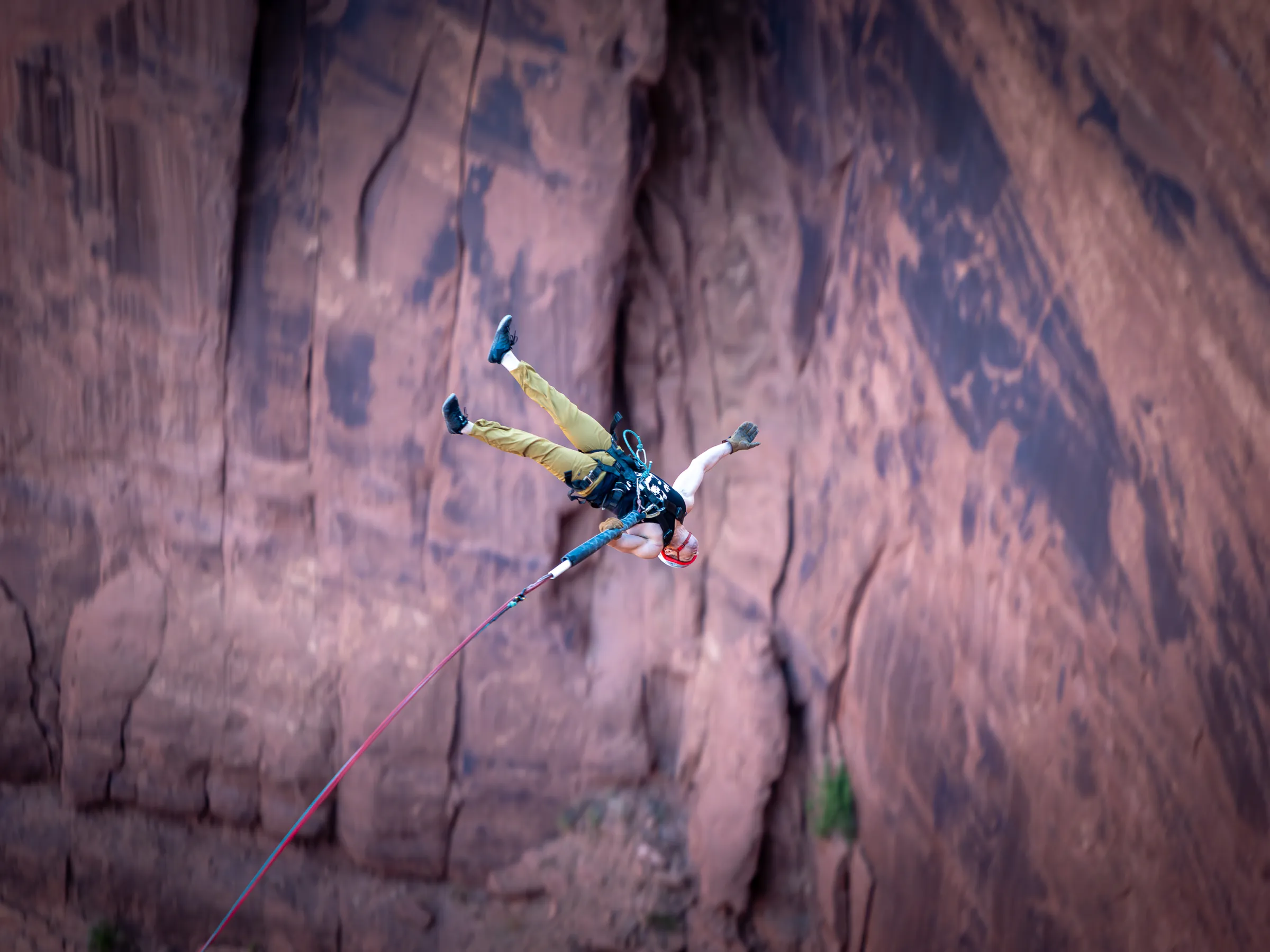 Person with harness bungee jumping against a rocky cliff background.