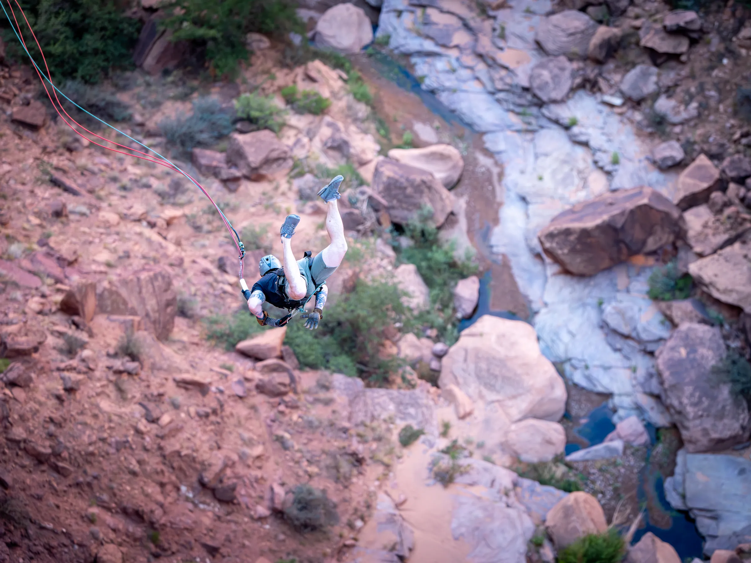 Person with helmet and harness jumping above rocky canyon.