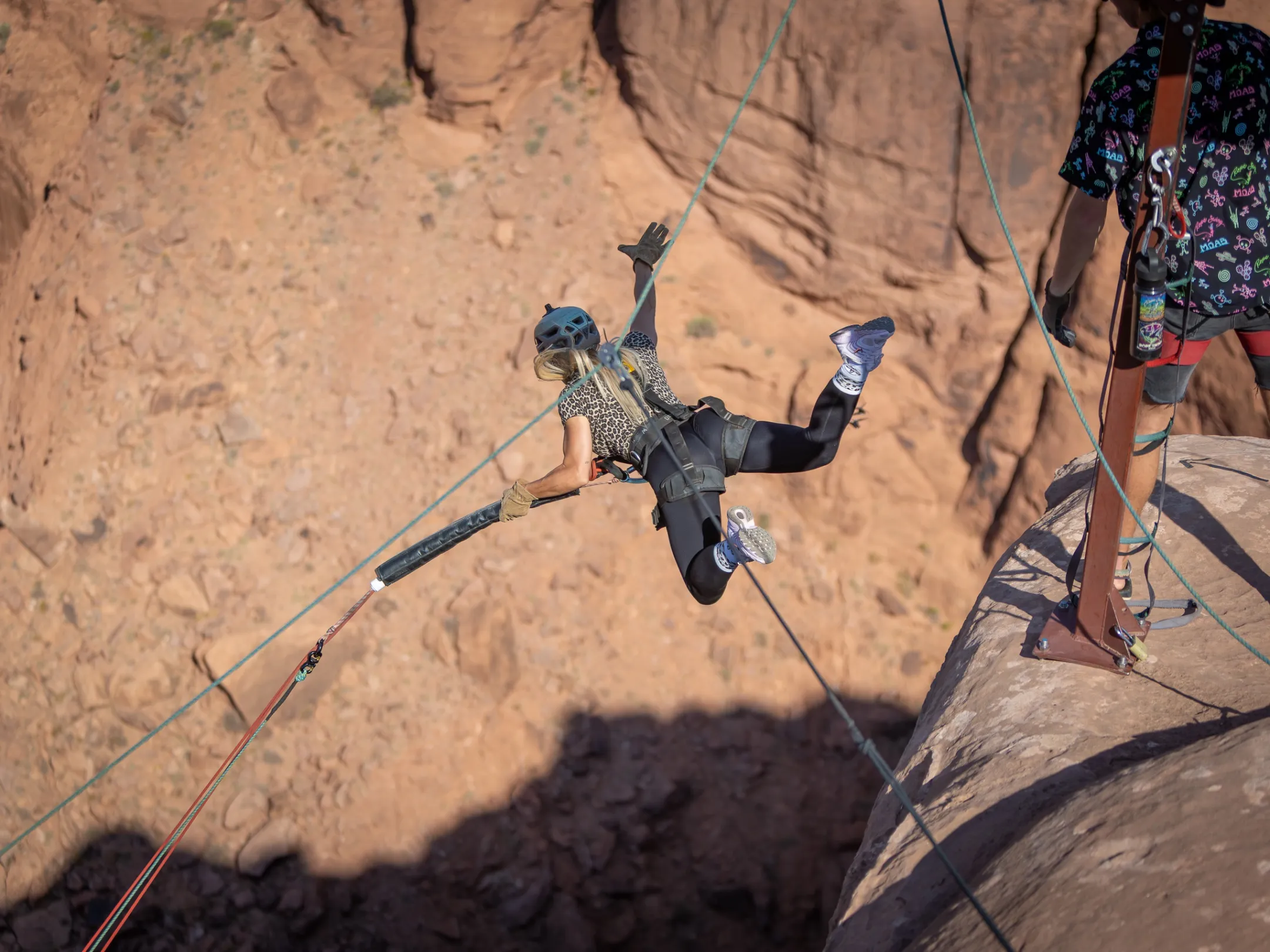 Person in climbing gear swings from a rock edge over a canyon.