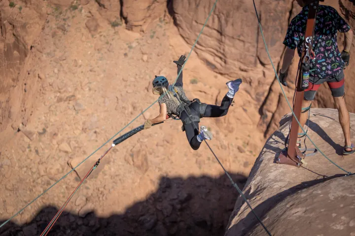 Person in climbing gear swings from a rock edge over a canyon.