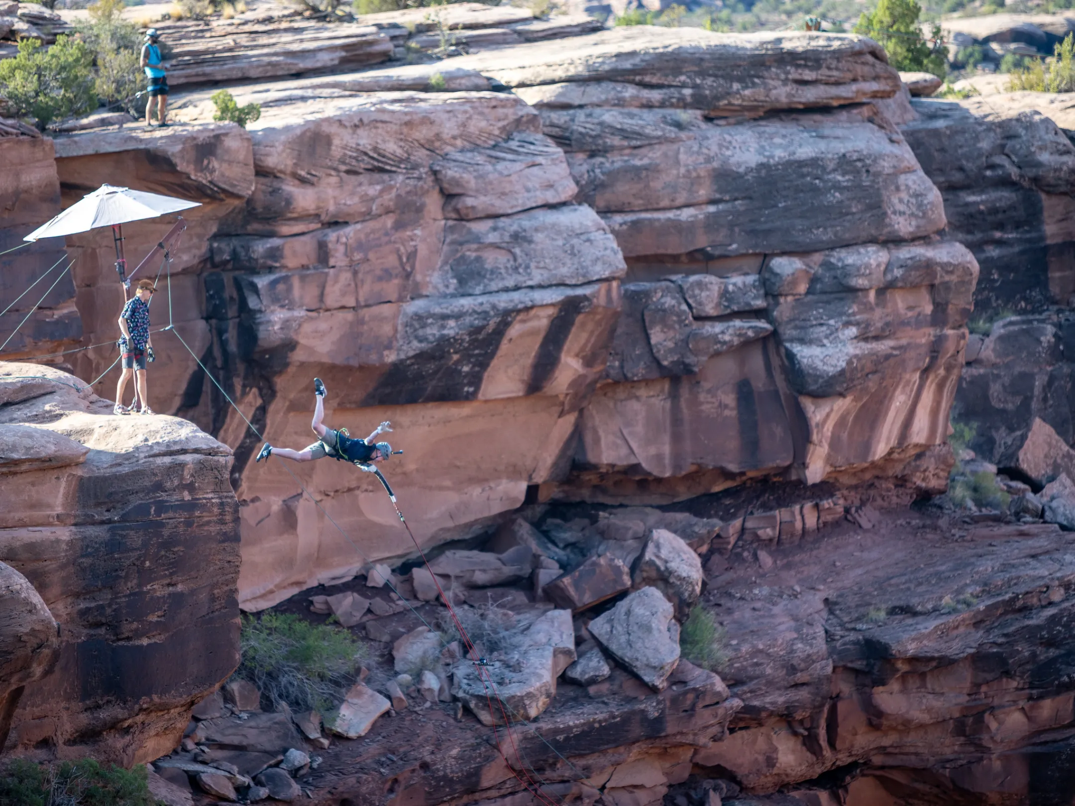 Person swings on a rope between rocky cliffs under a small umbrella structure.