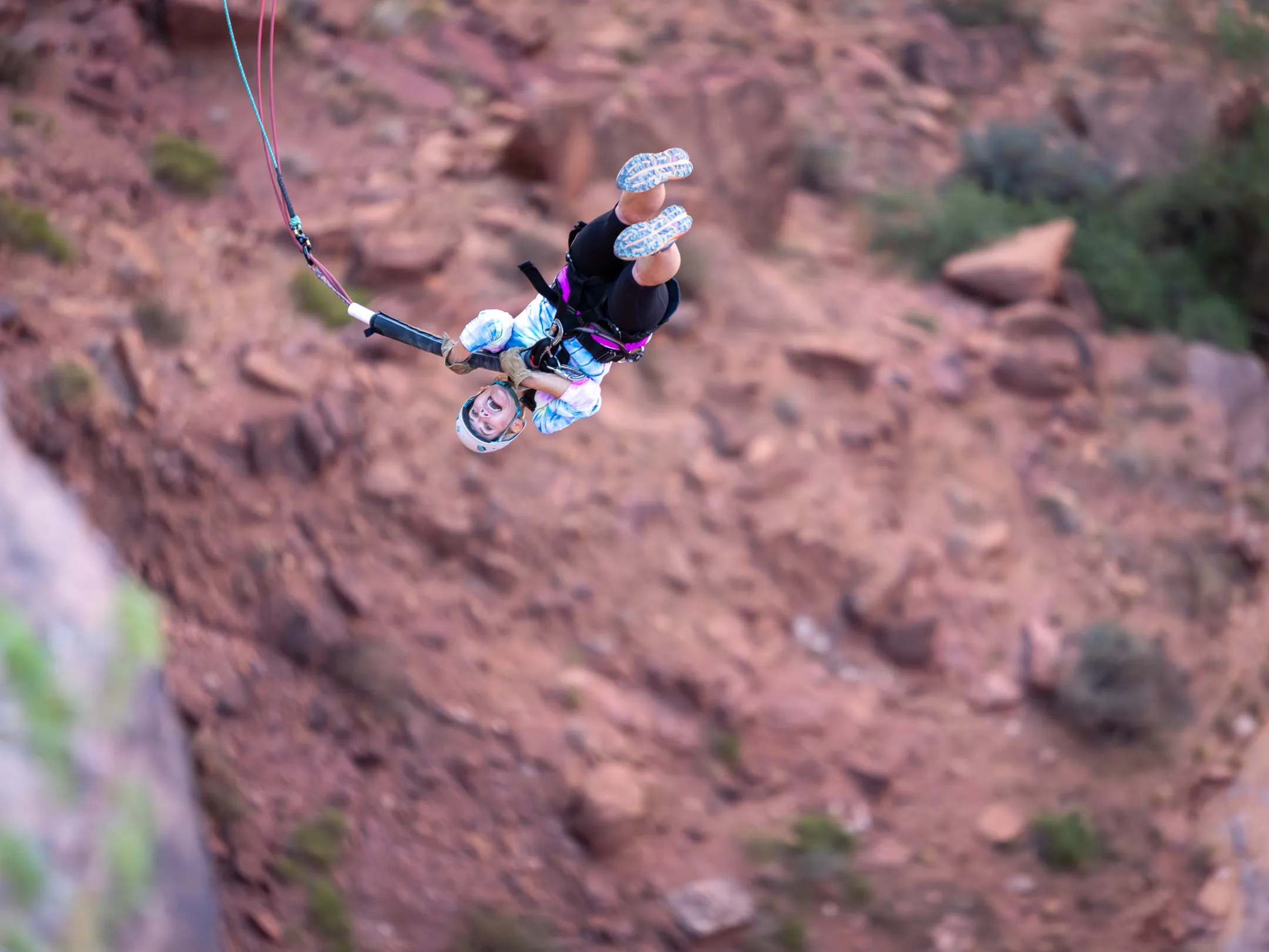 Person upside down bungee jumping over a rocky landscape with harness and helmet.