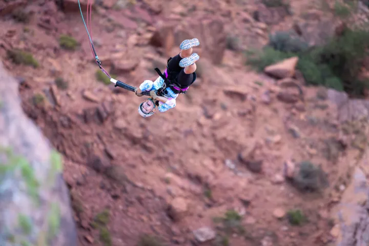 Person upside down bungee jumping over a rocky landscape with harness and helmet.
