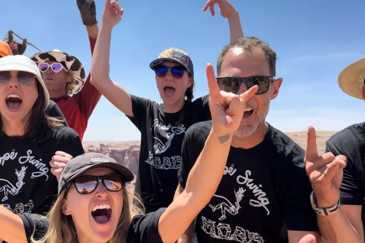 Group of excited people outdoors wearing sunglasses and matching 'Rope Swing' shirts.