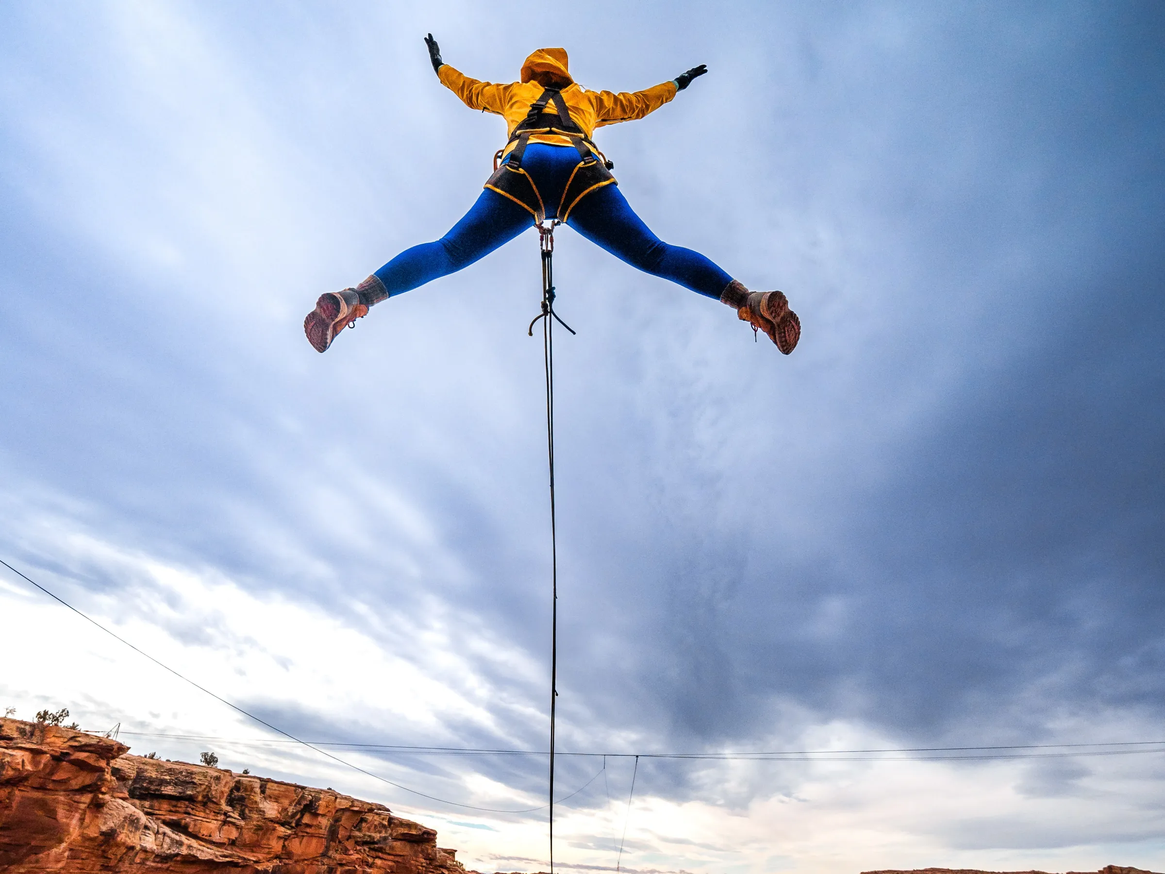 Person in yellow and blue bungee jumping over a canyon with cloudy sky in the background.