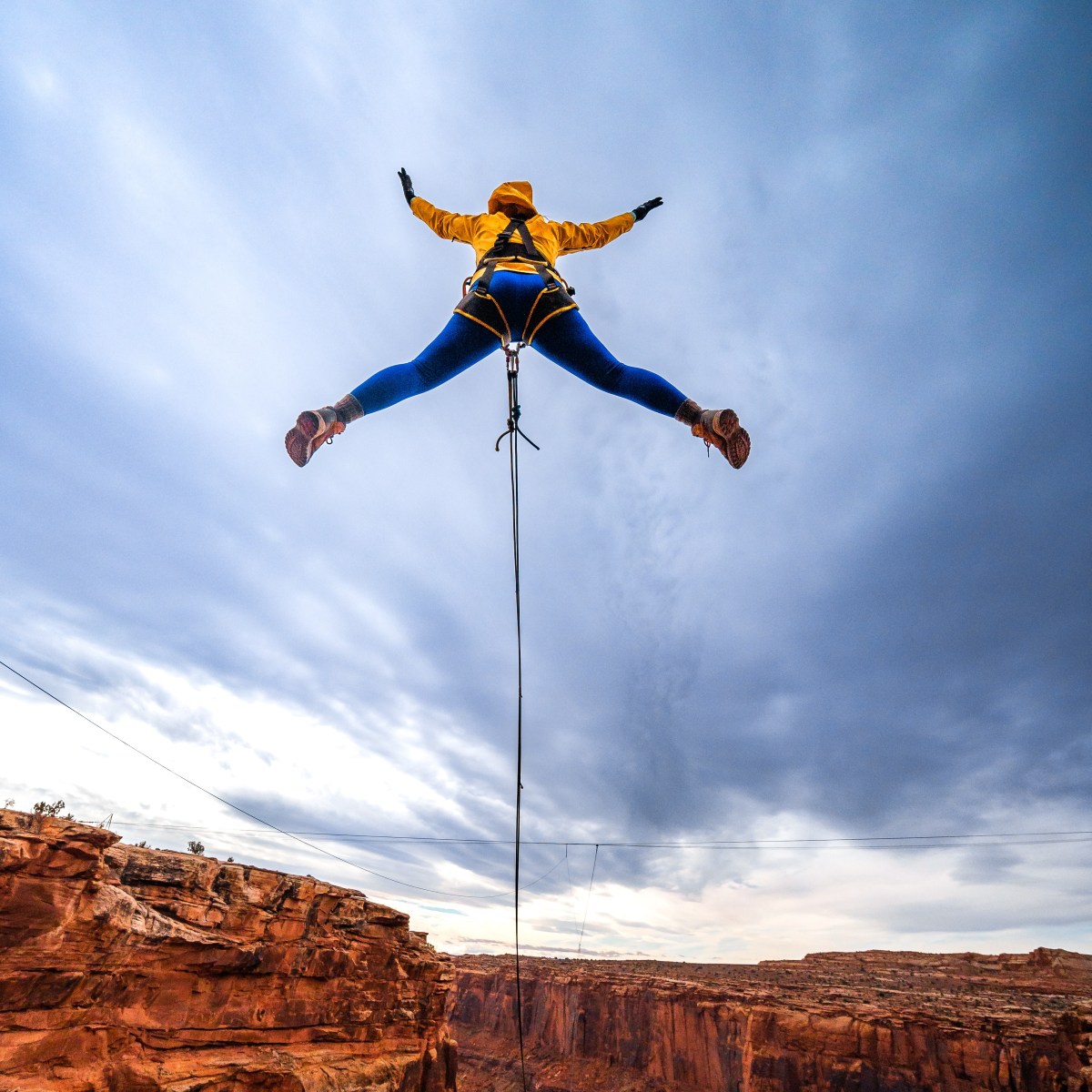 Person in yellow and blue bungee jumping over a canyon with cloudy sky in the background.