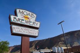 Sign for Moab Brewery with mountains and a clear blue sky in the background.