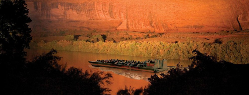 Boat with passengers on a river, canyon walls in the background during sunset.