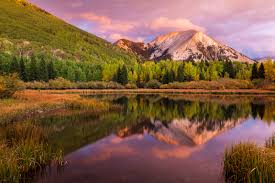 Mountain reflected in a calm lake with lush trees under a pinkish sunset sky.