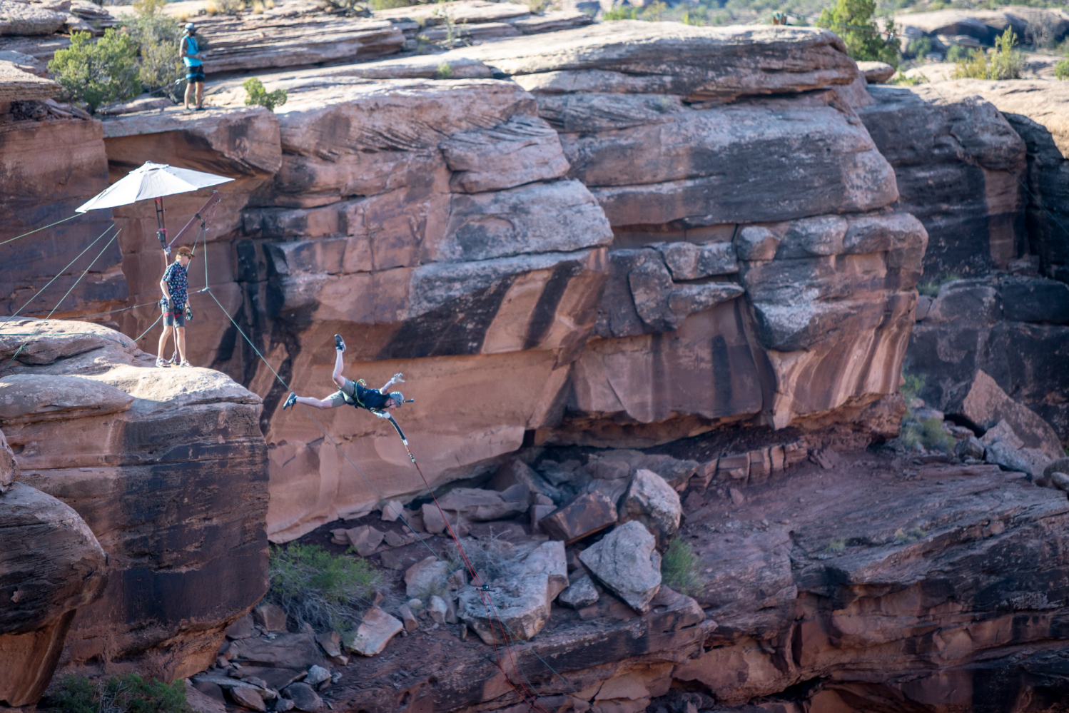 Person swings on rope over rocky canyon scene with onlookers.
