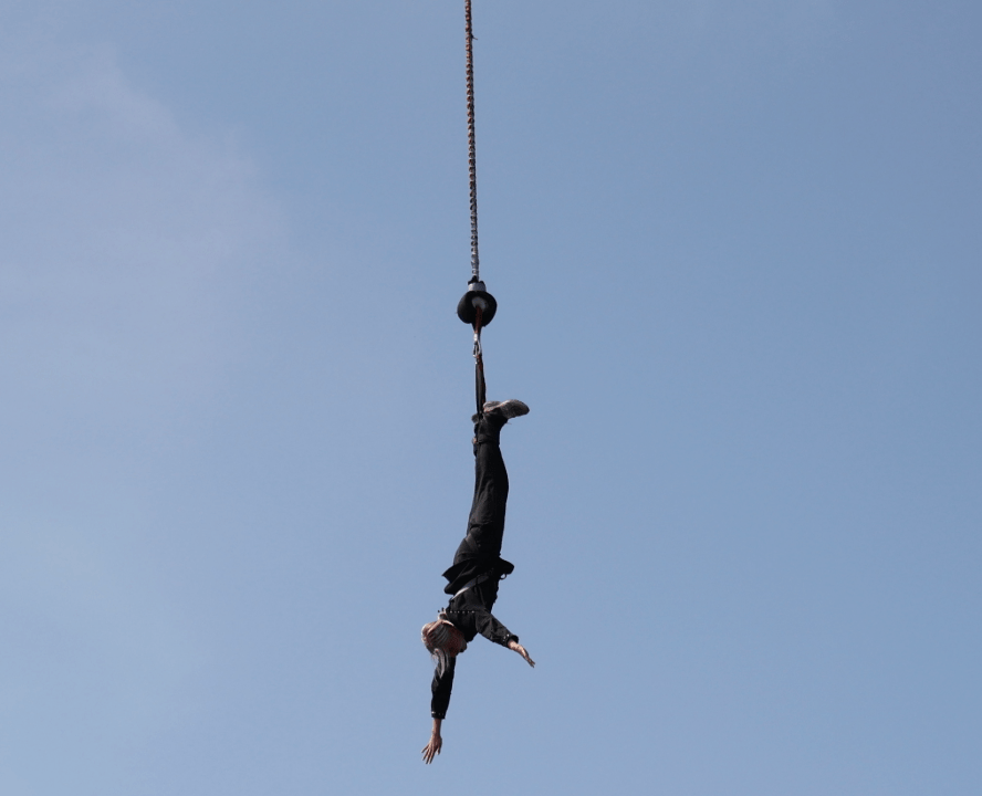 Person bungee jumping upside down against clear blue sky.