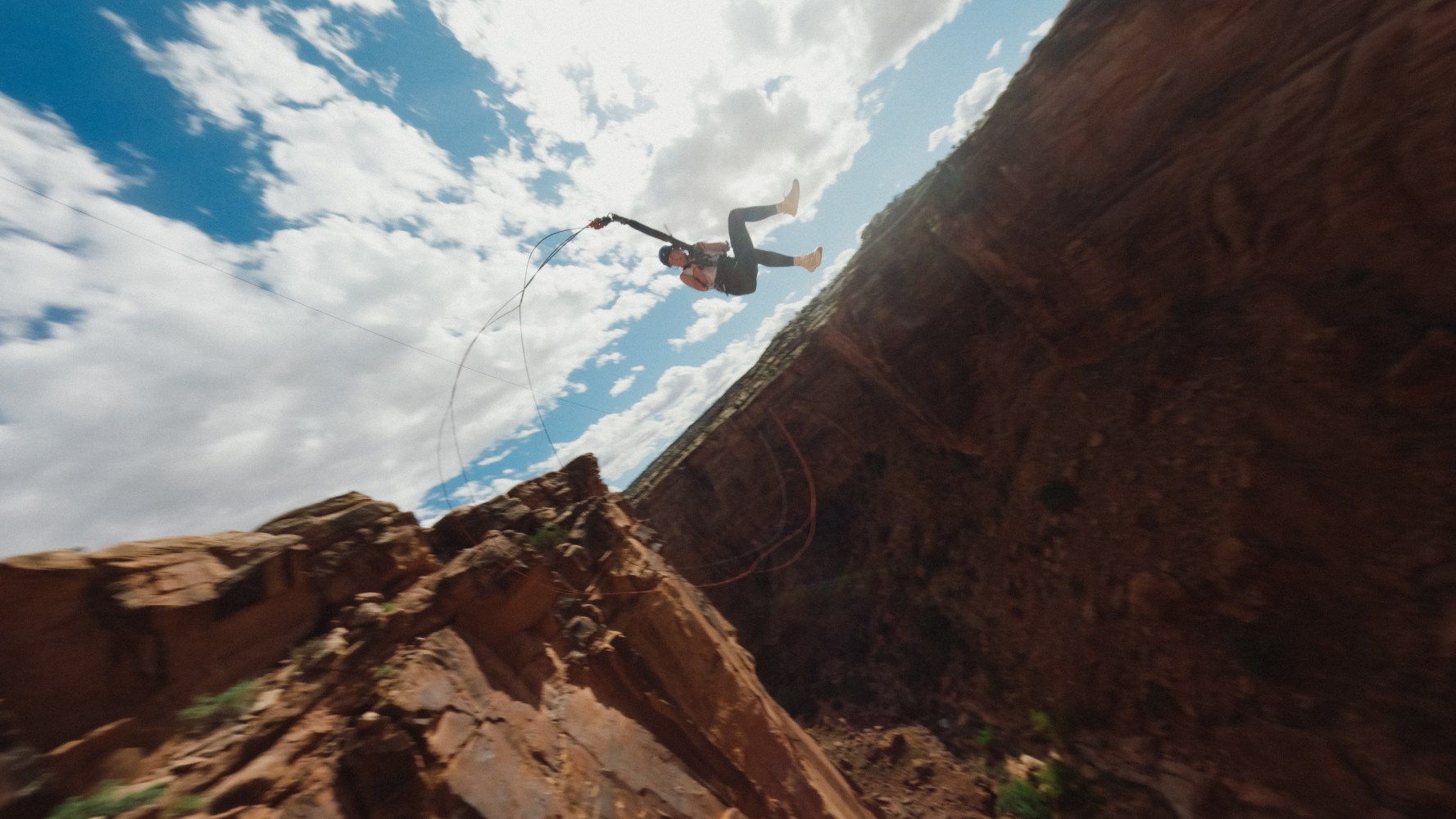Person swinging off cliffside against a sky with clouds.